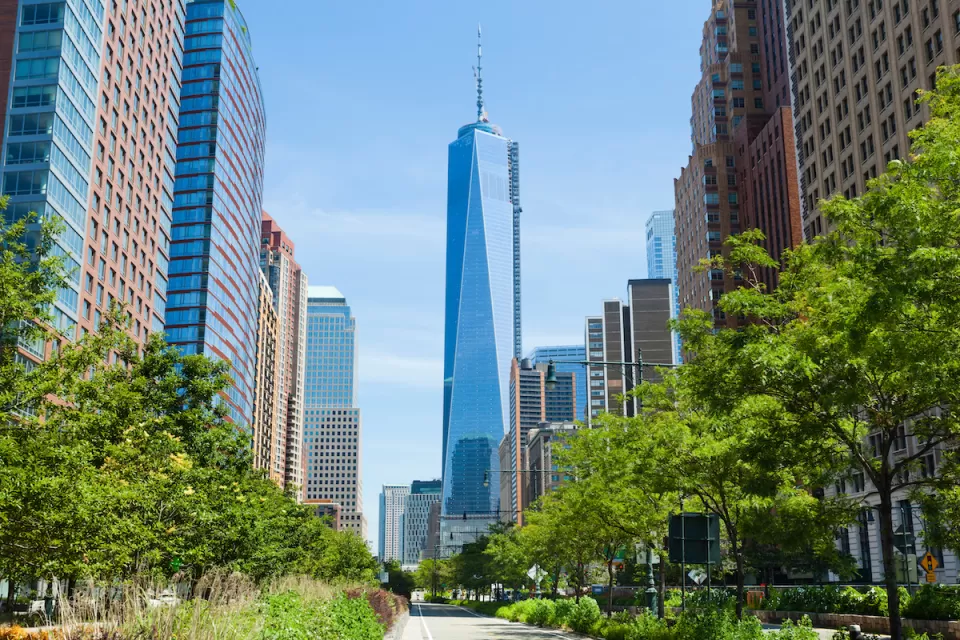 View of One World Trade Center down straight street with bright green trees on either side.